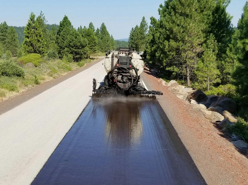 A machine is spraying asphalt on the side of a road
