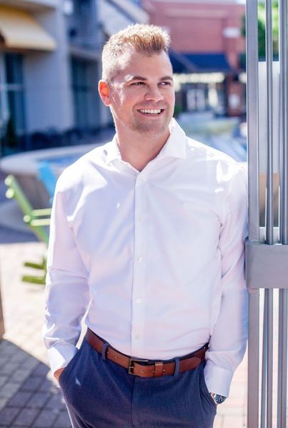 A man in a white shirt and blue pants is leaning against a fence.