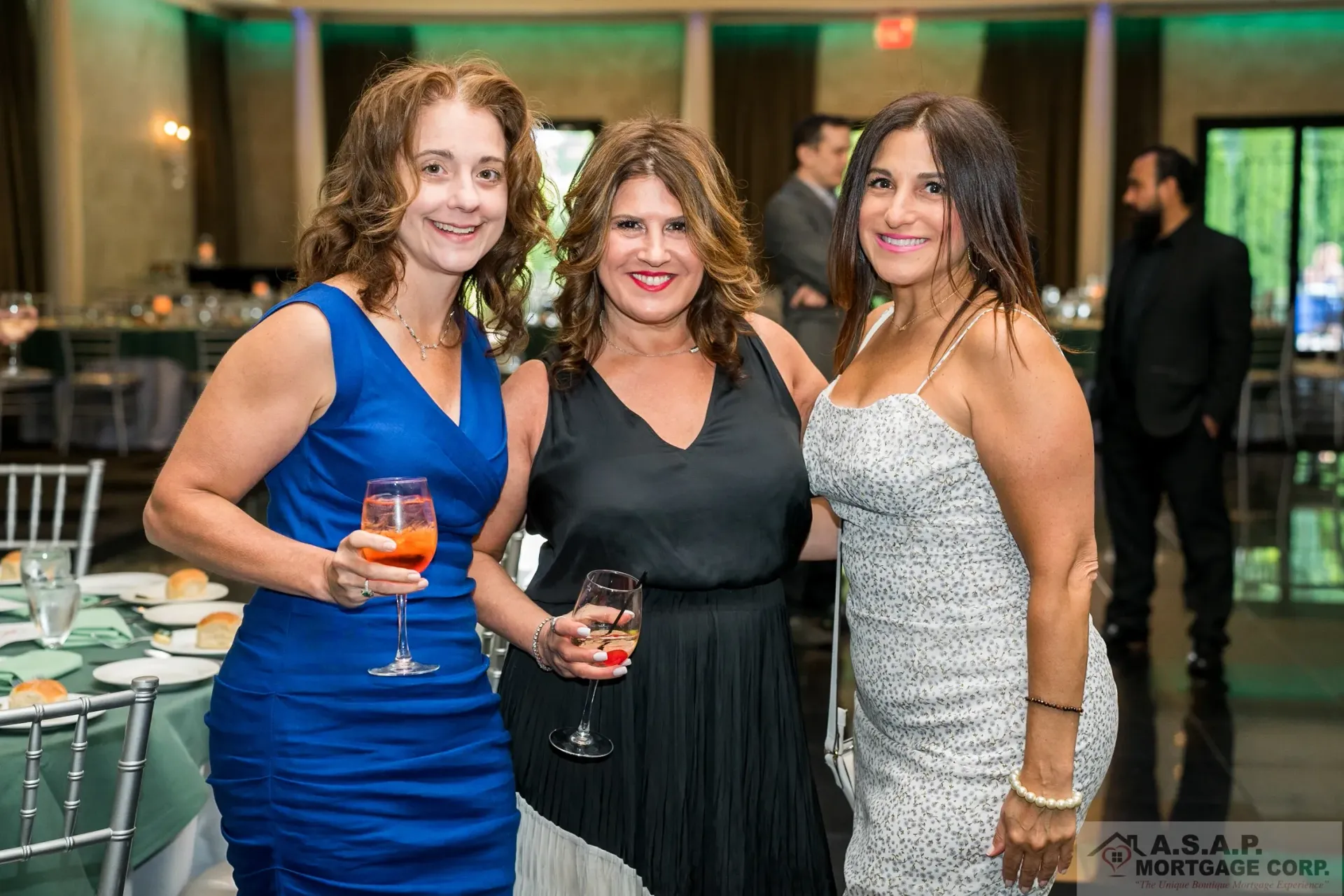 Three women are posing for a picture at a party while holding wine glasses.