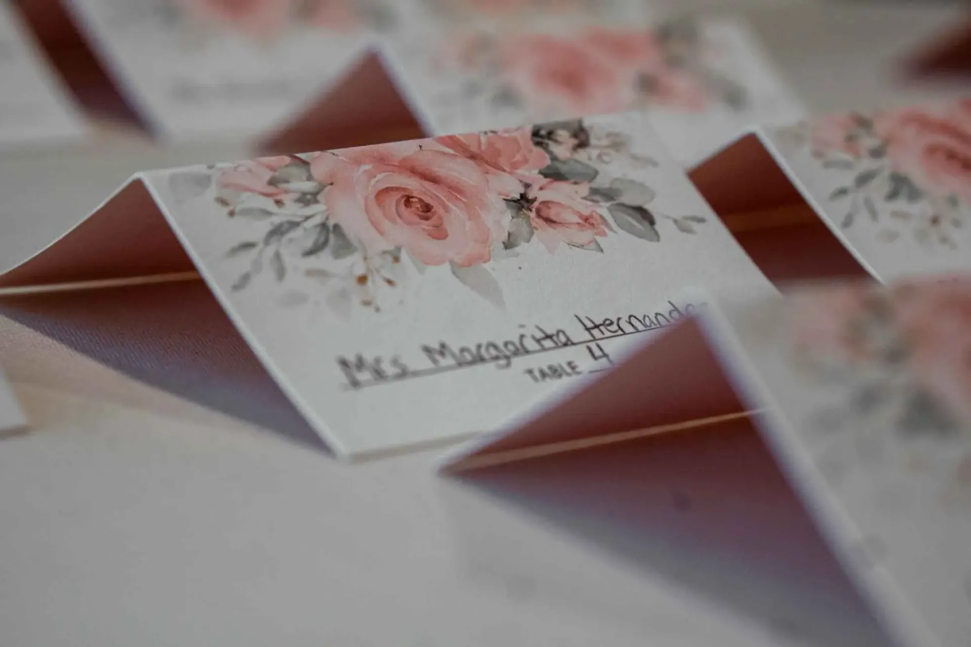 A row of place cards with pink roses on them are sitting on a table.