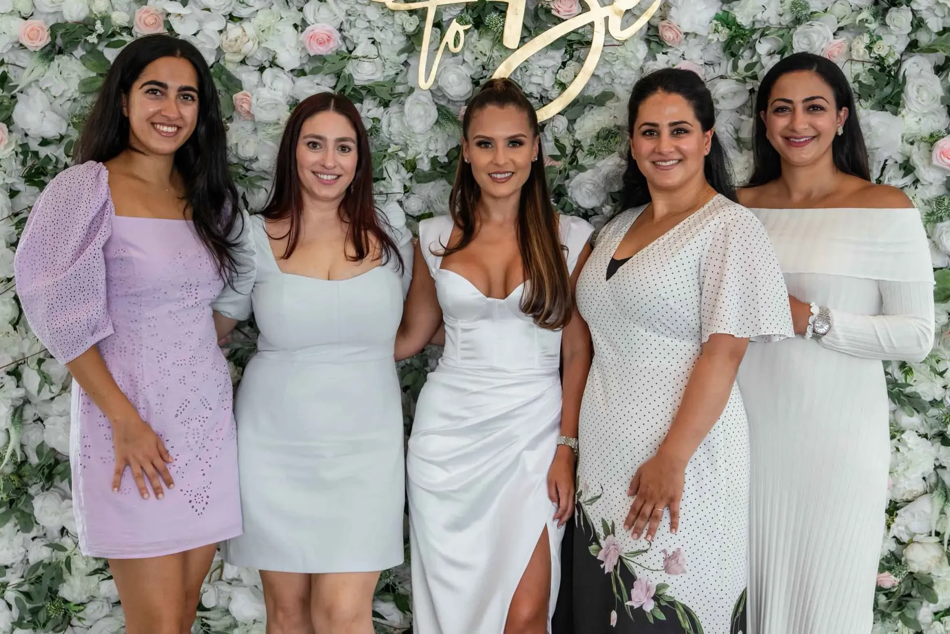 A group of women are posing for a picture in front of a flower wall.