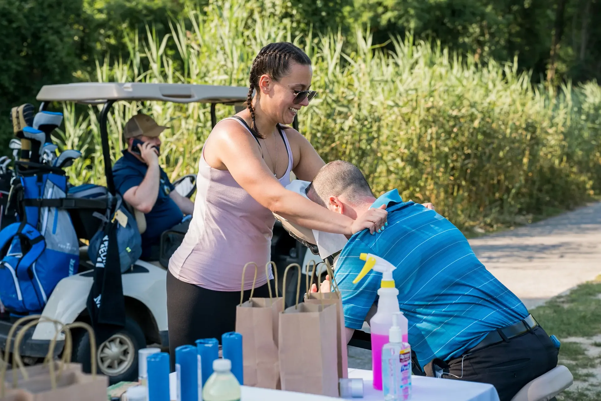 A woman is giving a man a massage in front of a golf cart.