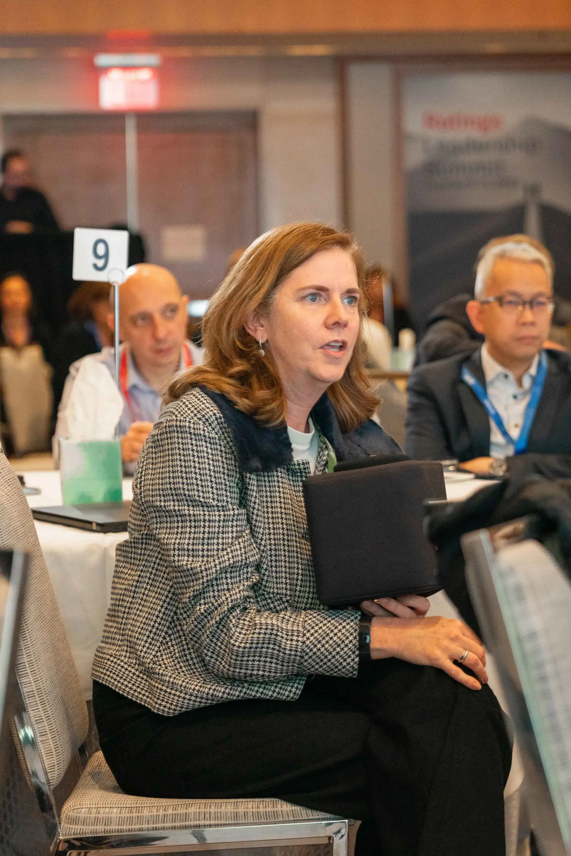 A woman is sitting in a chair at a conference holding a tablet.