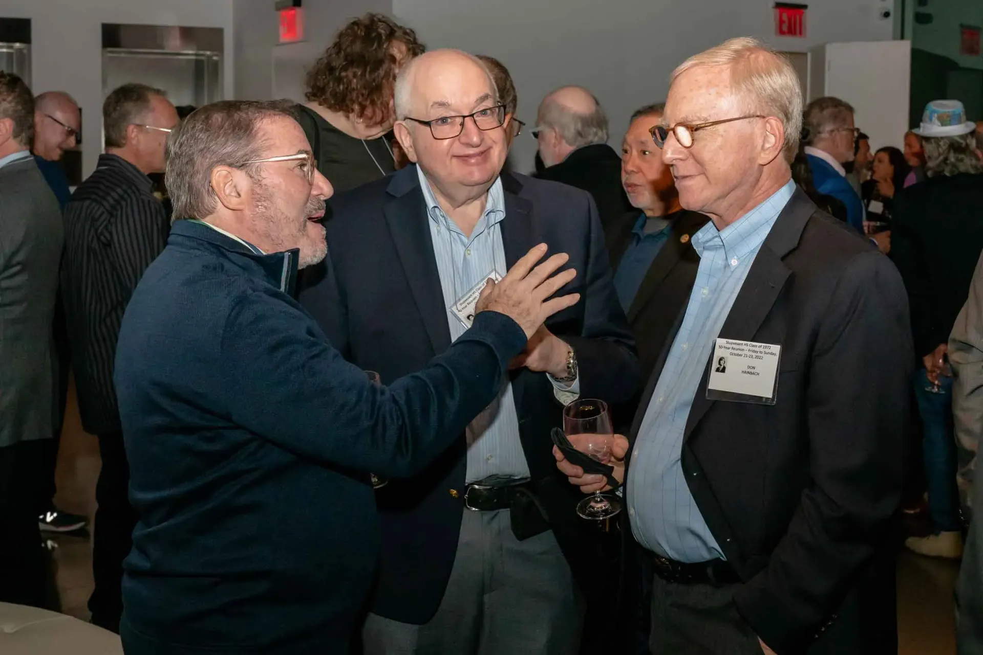 A group of men are standing in a room talking to each other.