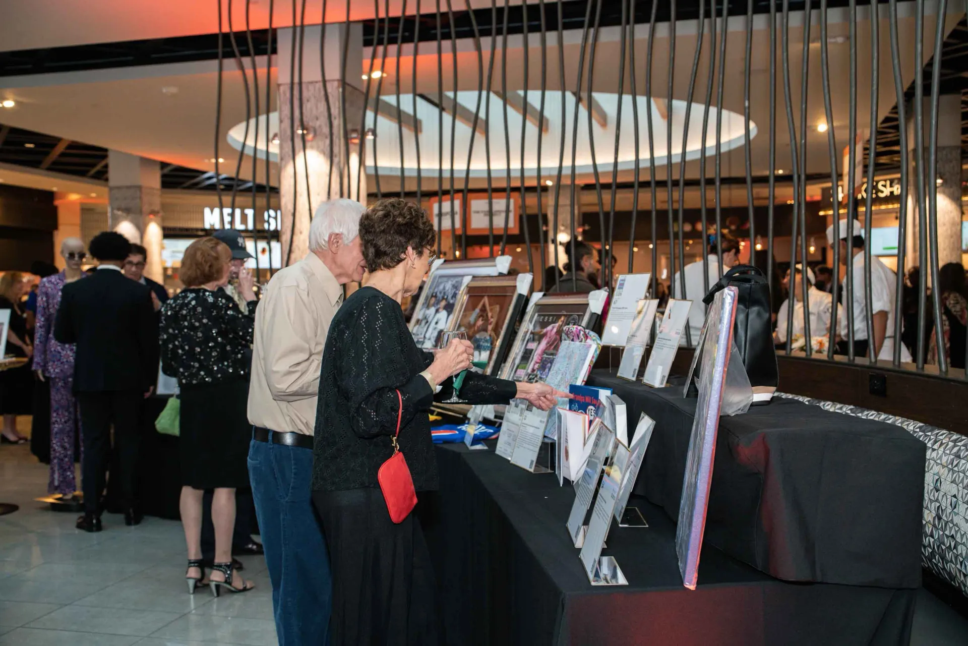 A group of people are standing around a table looking at paintings.