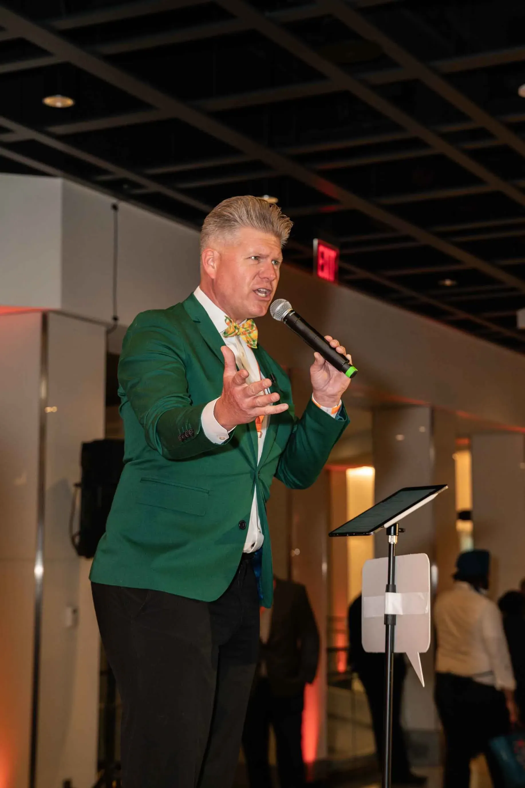 A man in a green jacket and bow tie is standing in front of a microphone.