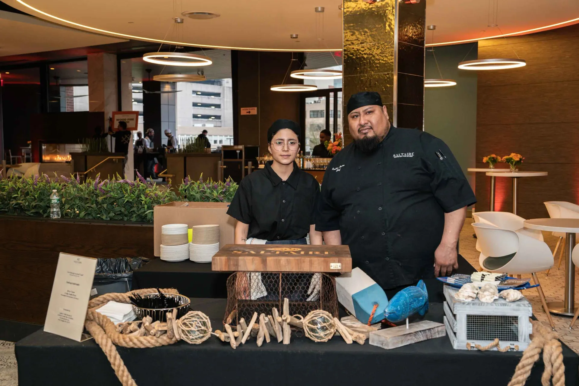 A man and a woman are standing in front of a table in a restaurant.
