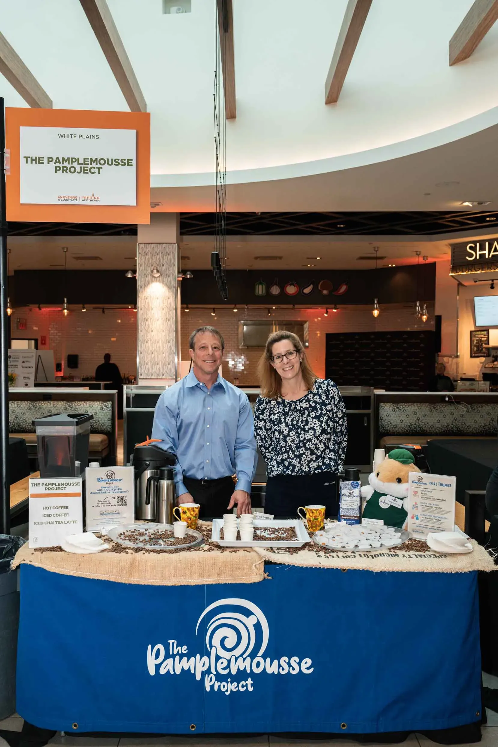 A man and a woman are standing in front of a table with a blue table cloth that says pamplemousse project.