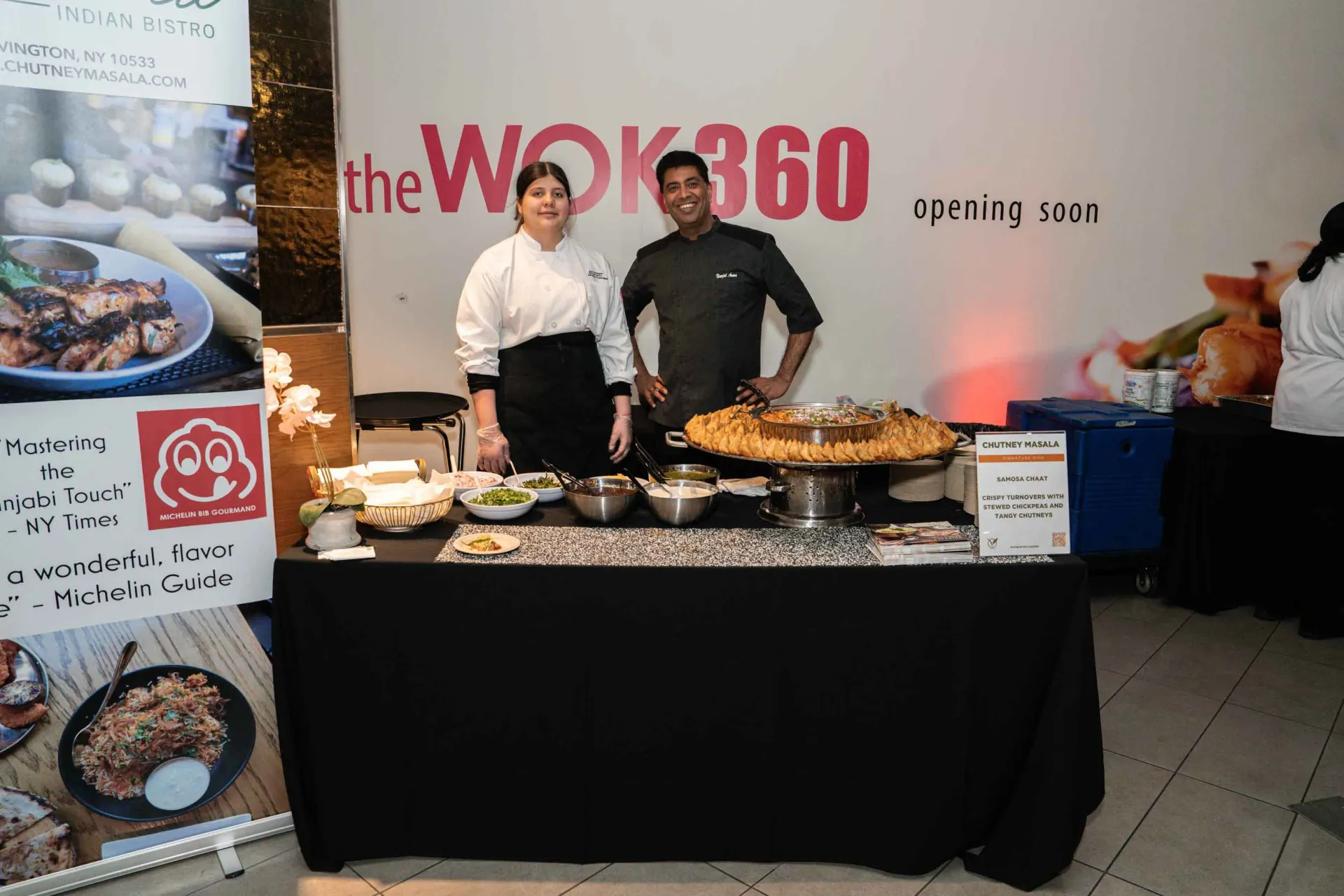A man and a woman are standing in front of a table with food on it.