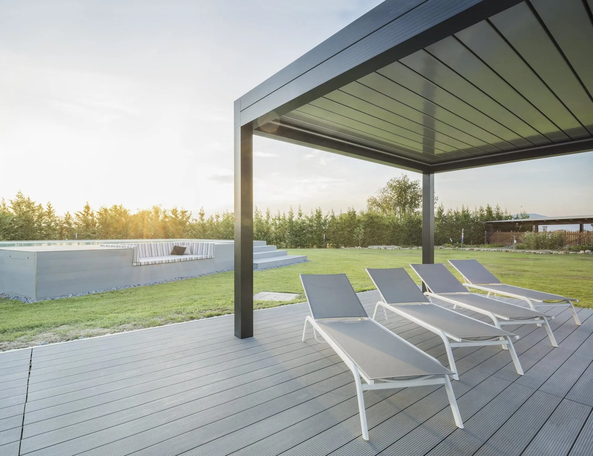 Moderno patio esterno con lettini prendisole sotto un pergolato, accanto a una piscina e a un prato.