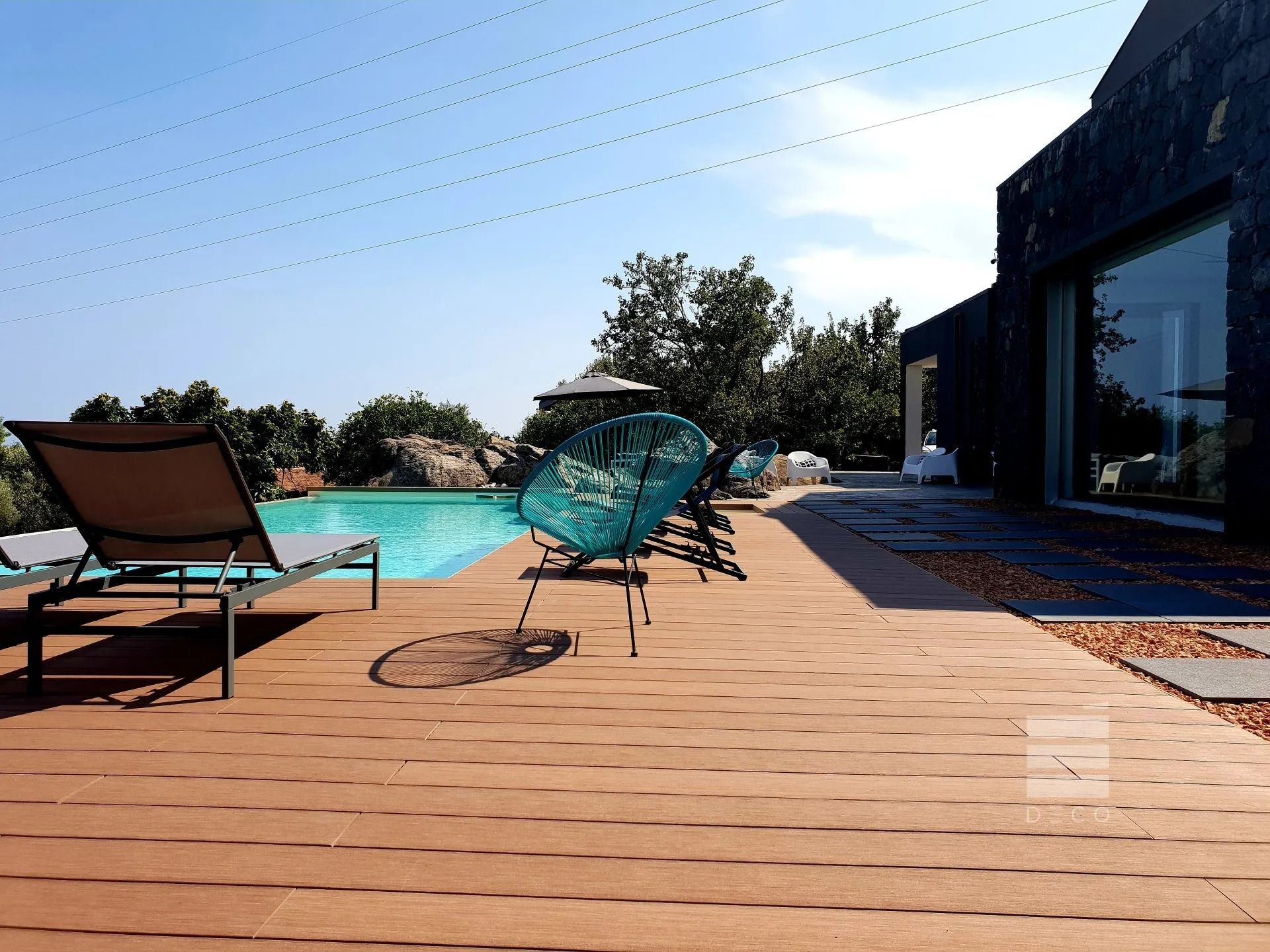 Terrazza a bordo piscina con sedie a sdraio, piscina e edificio moderno sotto un cielo limpido.