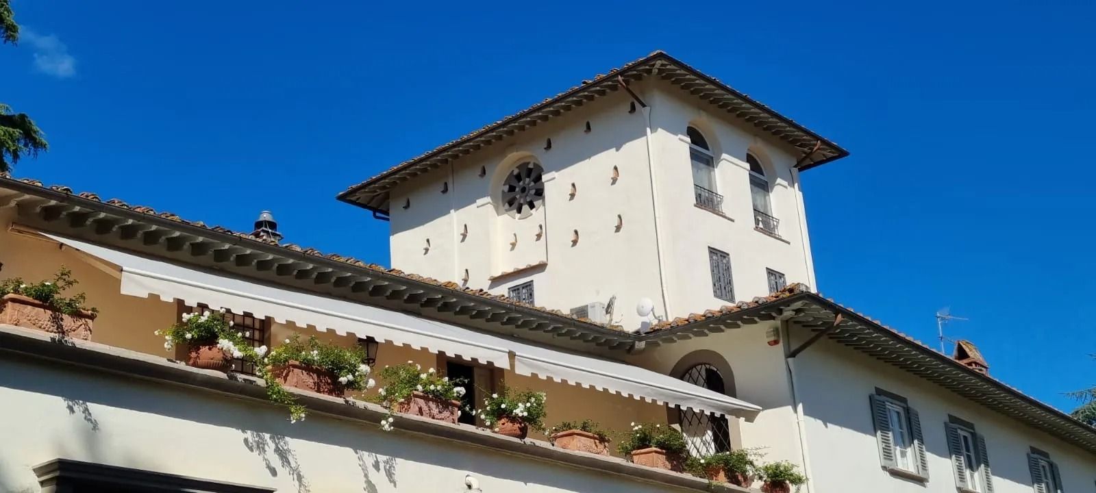 Un edificio bianco con una torre, un cielo azzurro e fioriere alle finestre.