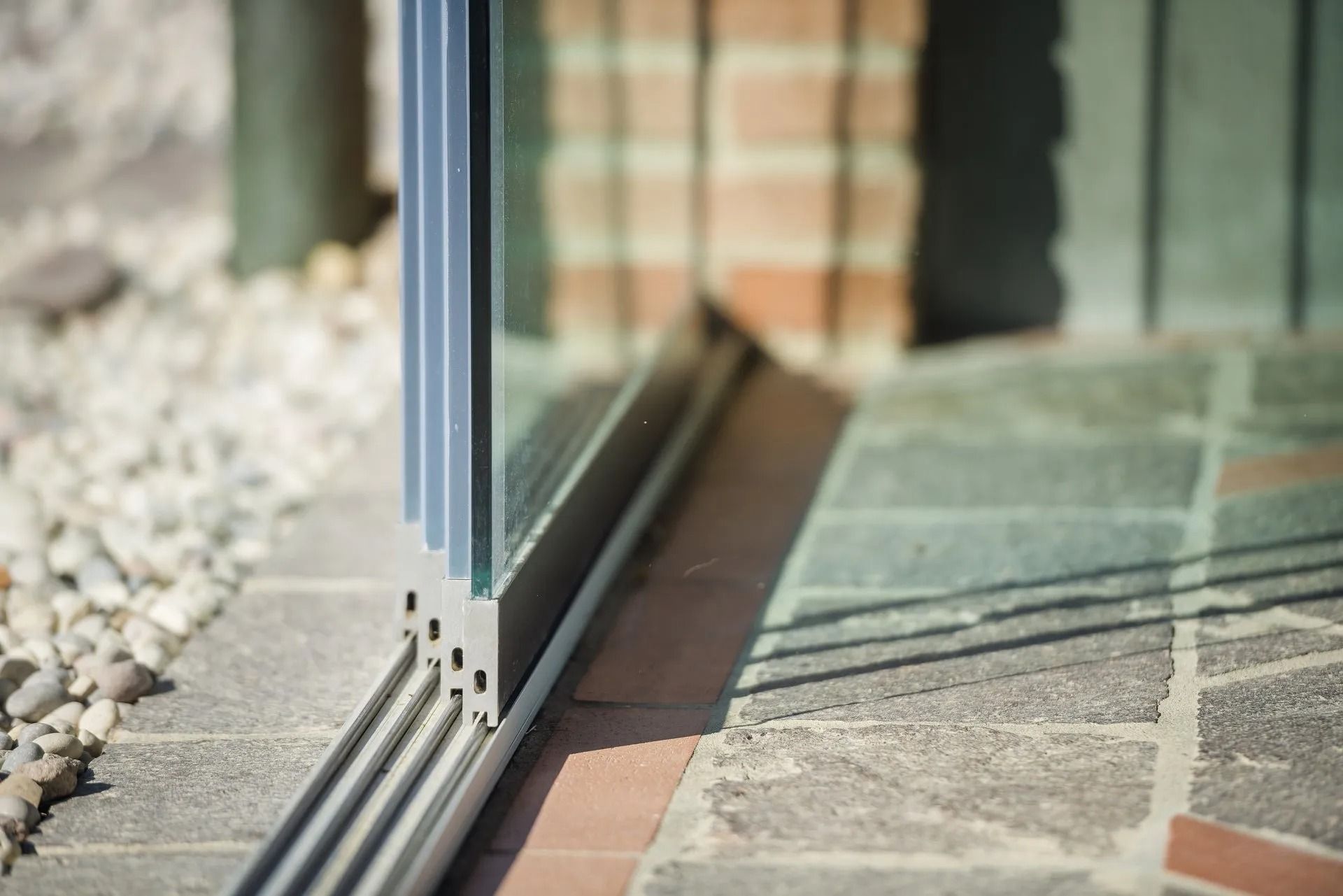 Telaio della porta scorrevole in vetro su patio in mattoni con ghiaia e muro di mattoni sullo sfondo.