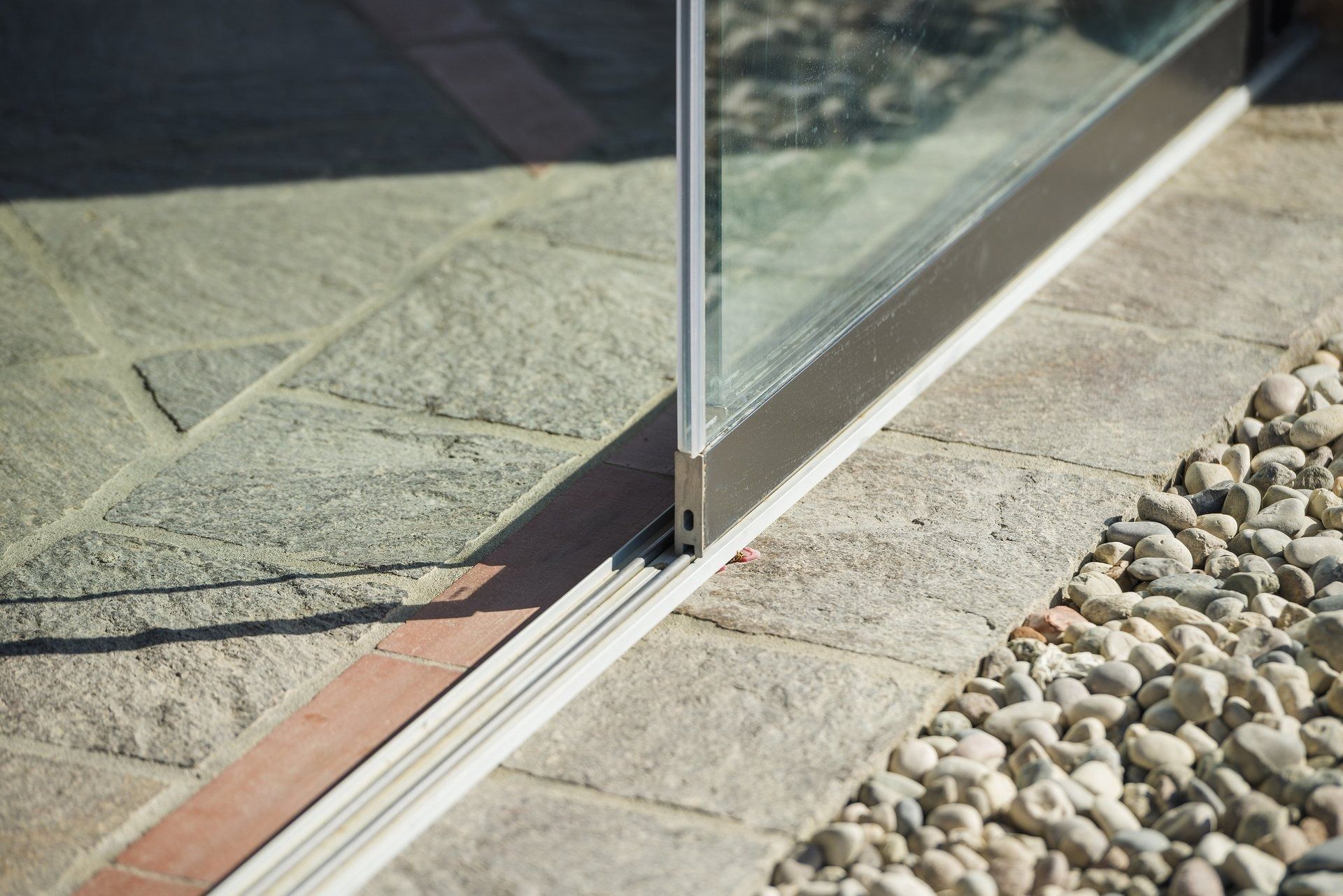 Porta scorrevole in vetro su un patio pavimentato con ciottoli sulla destra.