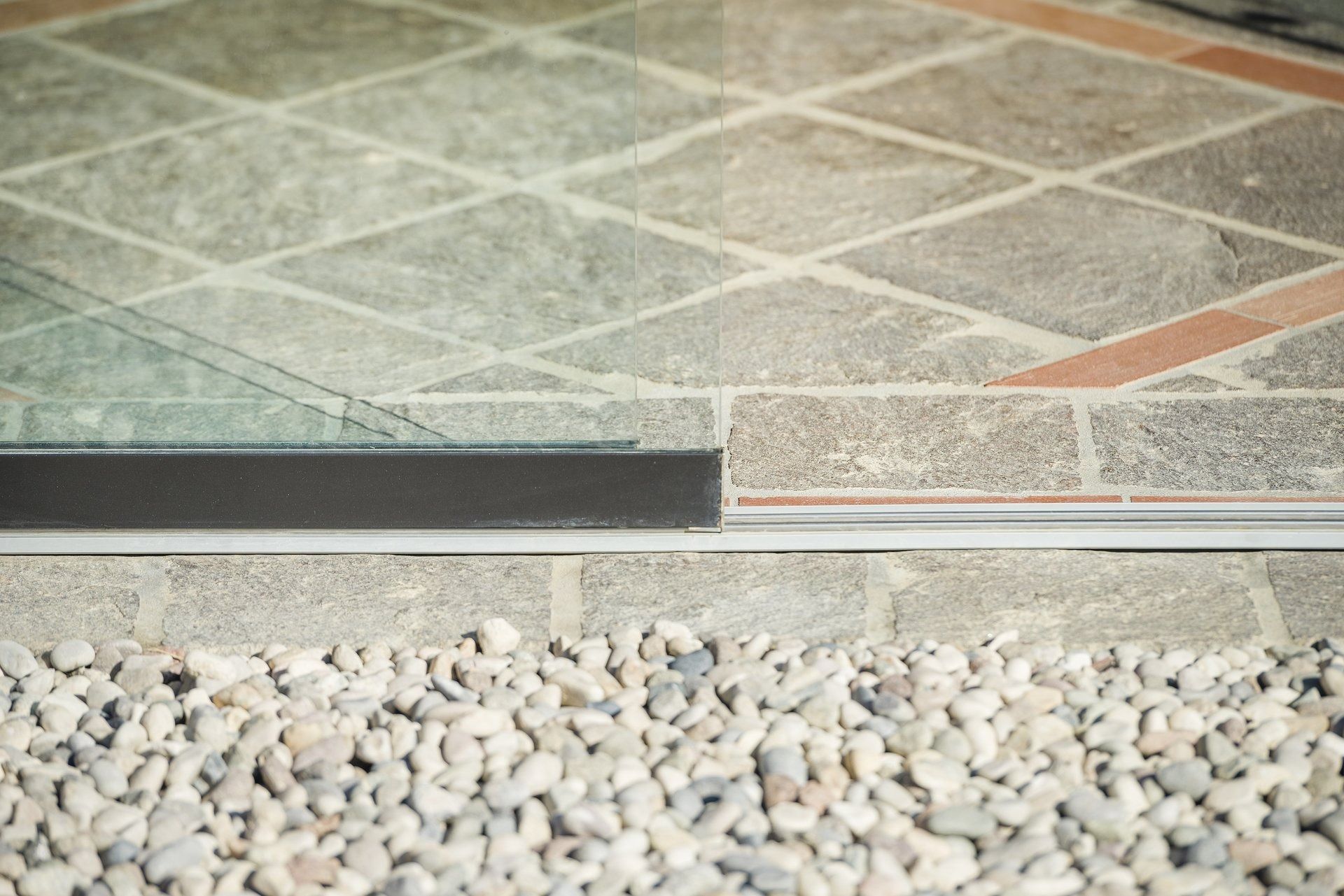 Guarnizione nera alla base della porta scorrevole in vetro sul patio in pietra con ghiaia.