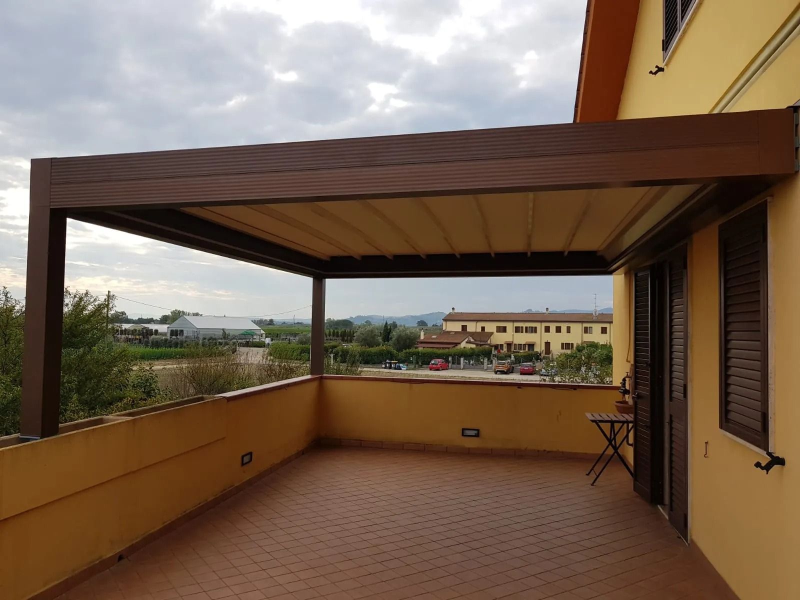 Pergola marrone con tettoia beige sopra una terrazza. La terrazza ha un pavimento color mattone.