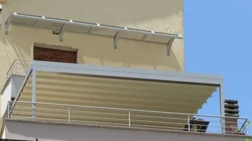 Tenda da sole retrattile bianca su un balcone con ringhiera in acciaio inossidabile; esterno dell'edificio beige.