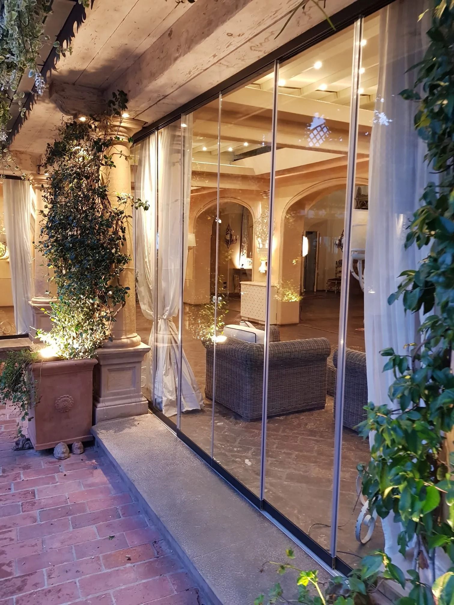 Patio esterno con pareti in vetro che riflettono lo spazio interno. Pavimento in mattoni