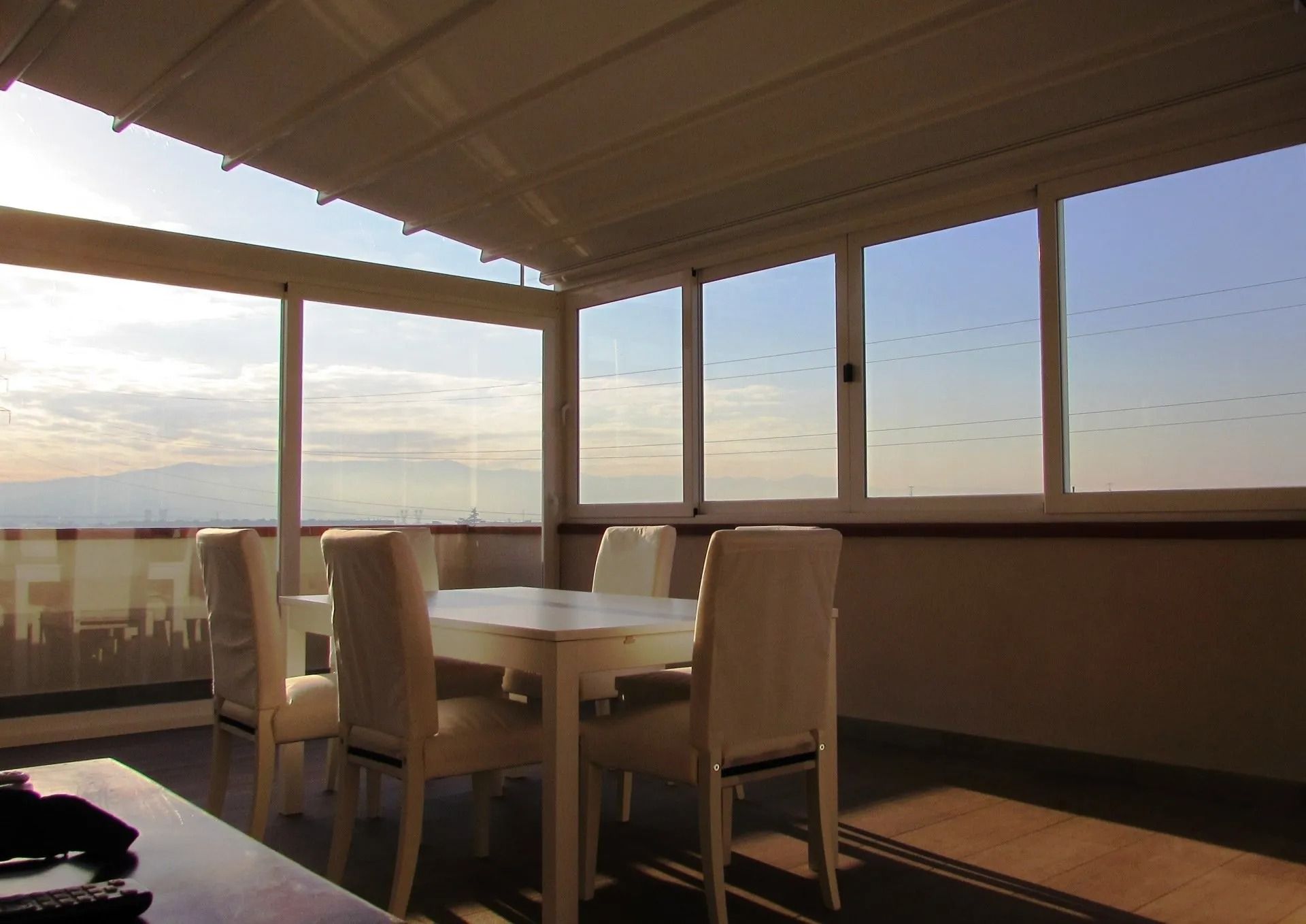 Patio recintato con mobili bianchi, con vista sul paesaggio urbano. Finestre soleggiate e tenda da sole bianca.
