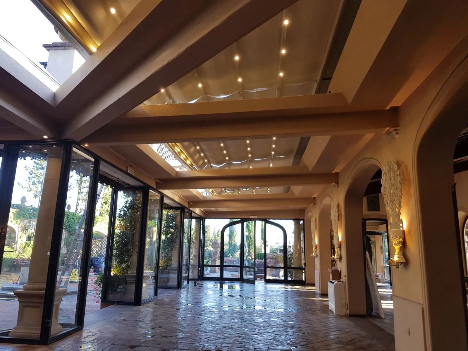 Spazio esterno coperto con pareti in vetro, porte ad arco e pavimento in piastrelle riflettenti.