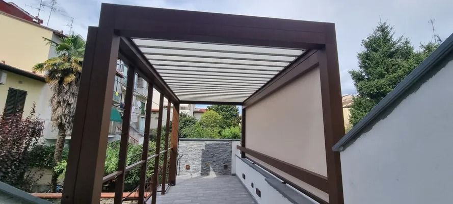 Un moderno pergolato marrone con tetto decorato e tenda laterale beige sopra un patio.