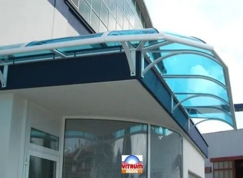 Tenda da sole curva e blu sopra l'ingresso di un edificio bianco. La tenda è sostenuta da una struttura in metallo bianco.