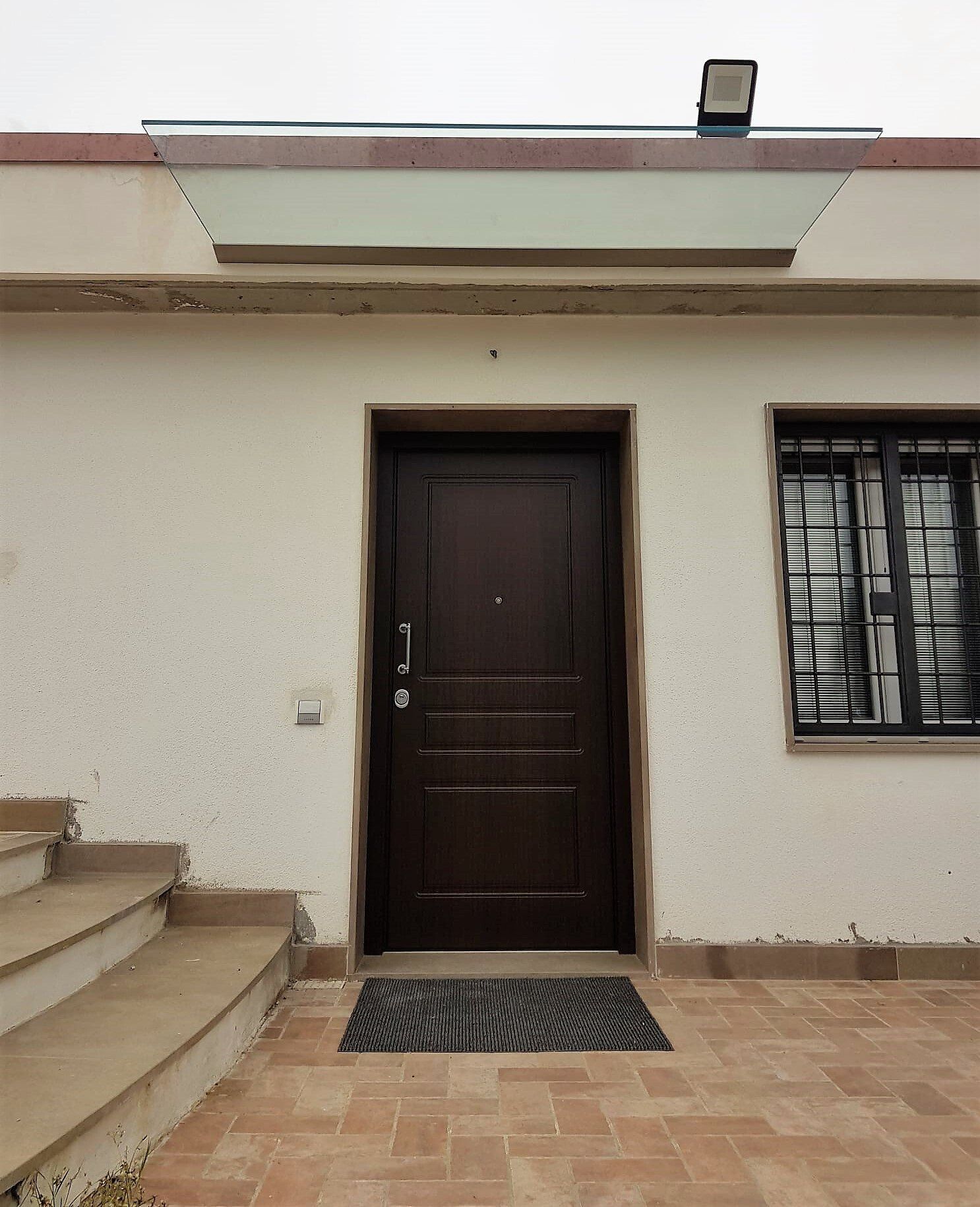 Vista esterna di un edificio con una porta marrone scuro, una finestra con le sbarre e gradini