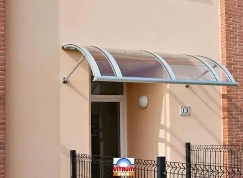 Tenda ad arco con cornice bianca sopra una porta, a protezione dell'ingresso. Esterno dell'edificio con una parete
