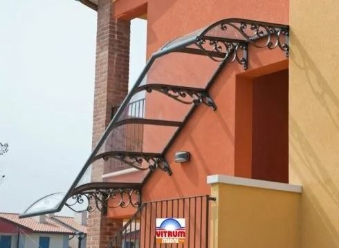 Tenda da sole in ferro battuto e vetro sopra una porta di un edificio arancione e giallo.