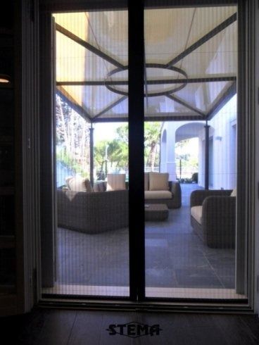 Porta a zanzariera in un ingresso che conduce al patio esterno arredato, sotto una struttura coperta.