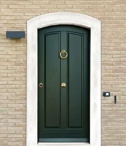 Porta d'ingresso verde con batacchio e finiture in ottone, inserita in un muro di mattoni chiari.