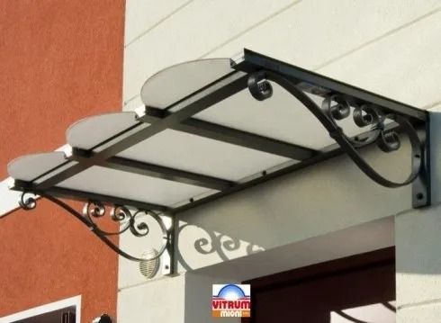 Tenda da sole trasparente e decorata in metallo nero sopra un portone, collegata a un edificio di colore chiaro