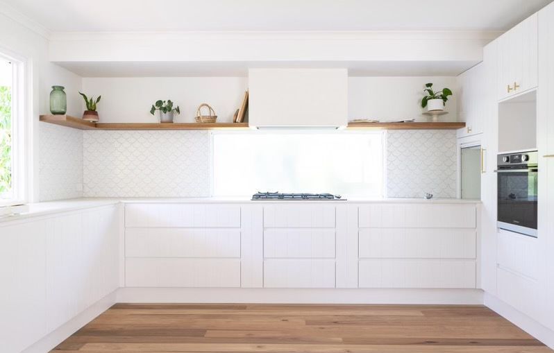 White kitchen with wood shelves, cabinets, and light wood floors.