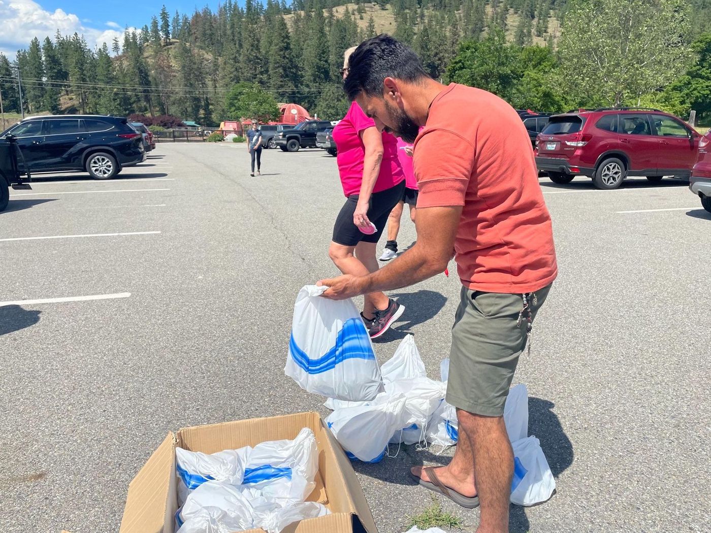 A man is standing next to a box of plastic bags in a parking lot.