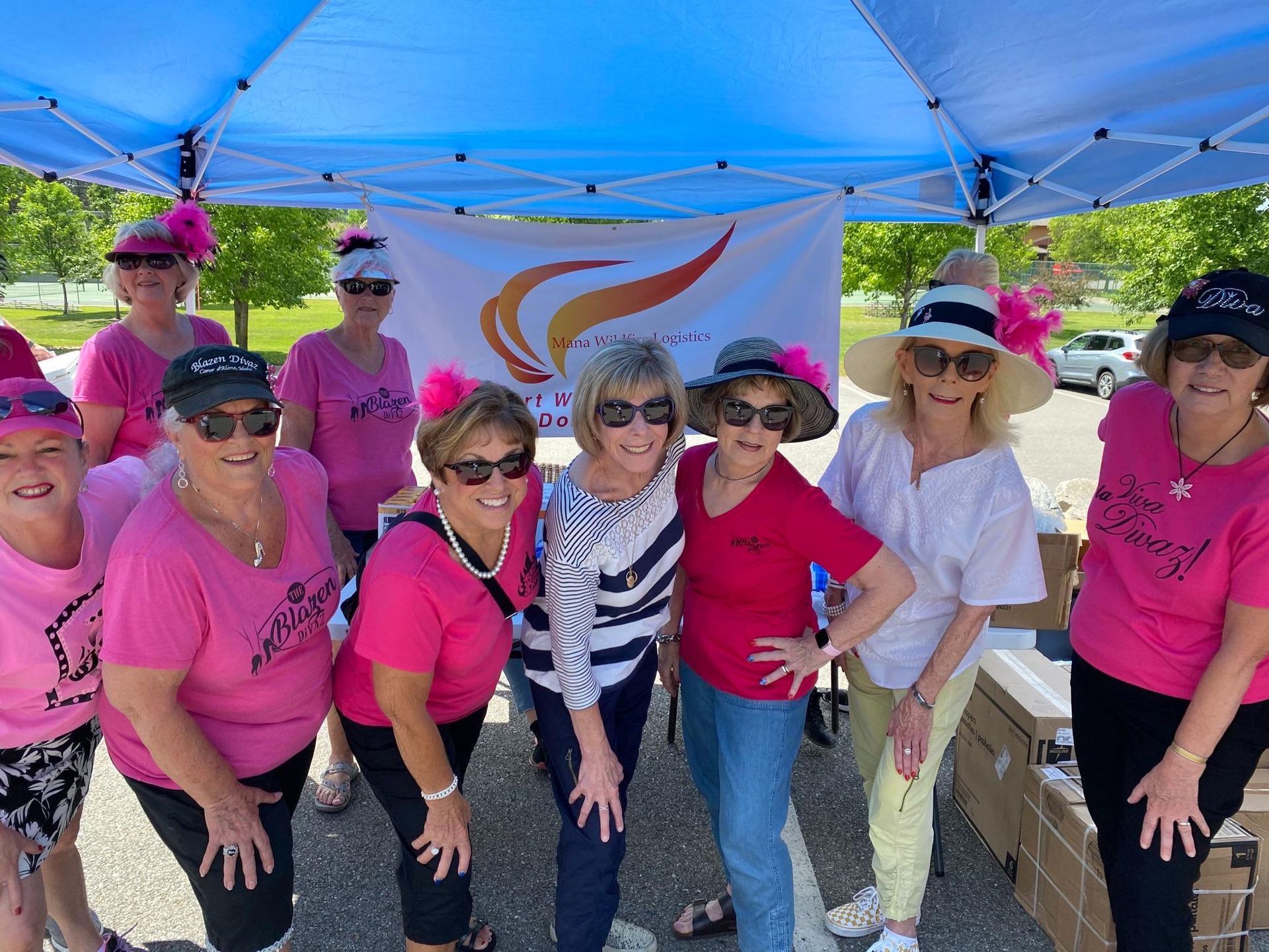 A group of women are posing for a picture under a blue tent.