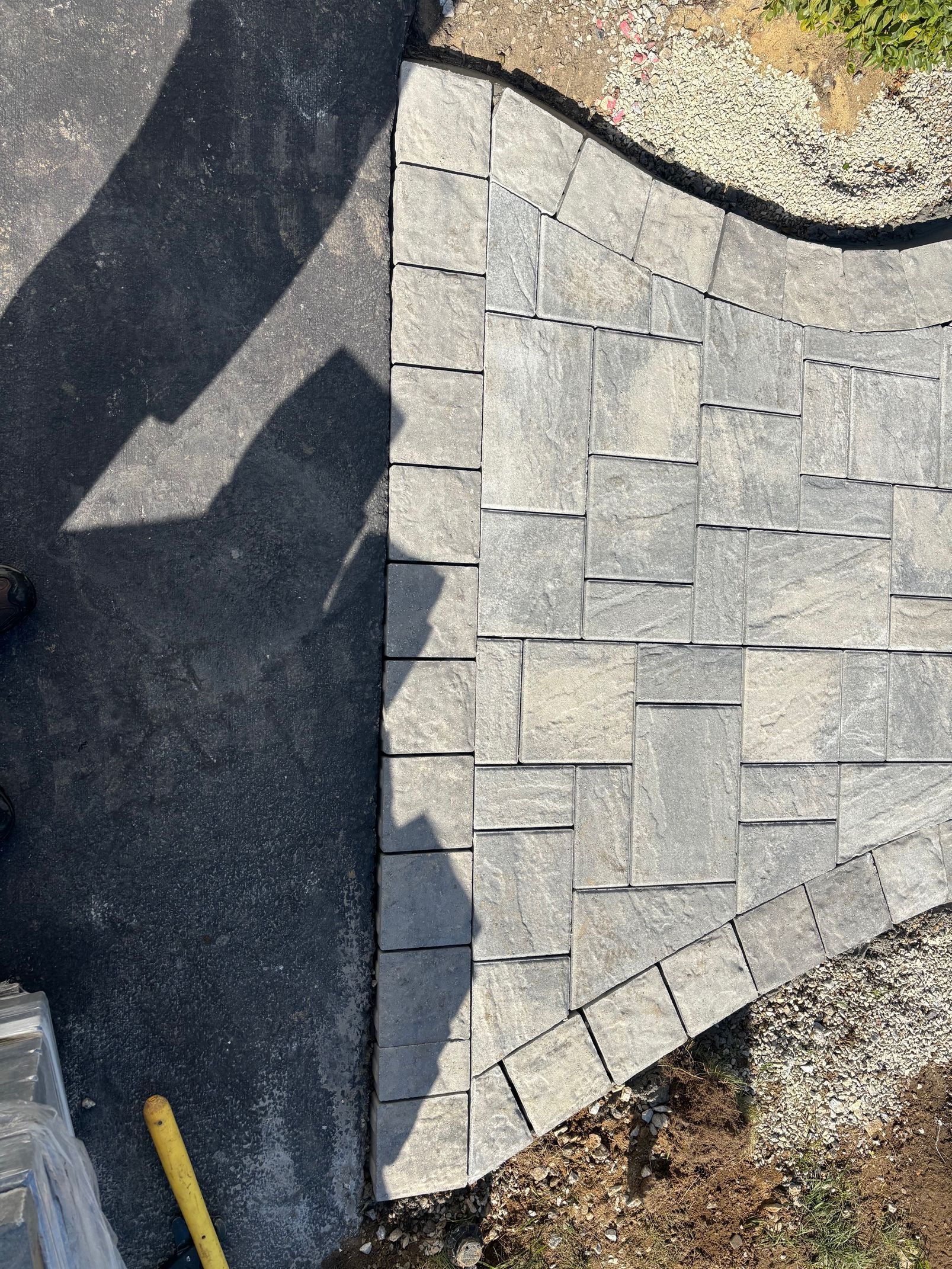 Asphalt driveway meets a gray paver walkway with a curved edge.