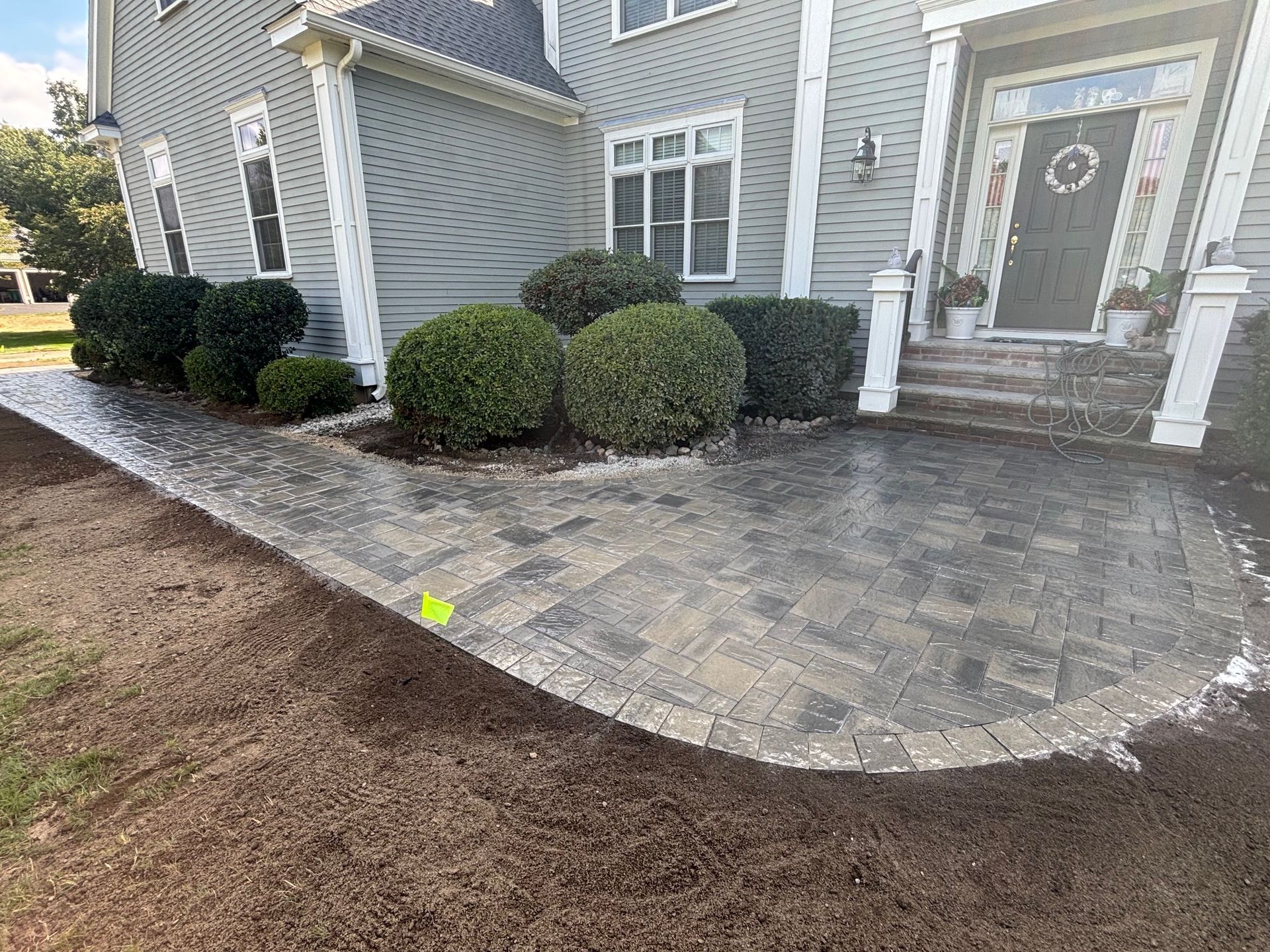 Curved brick walkway leading to a house with shrubs and steps.