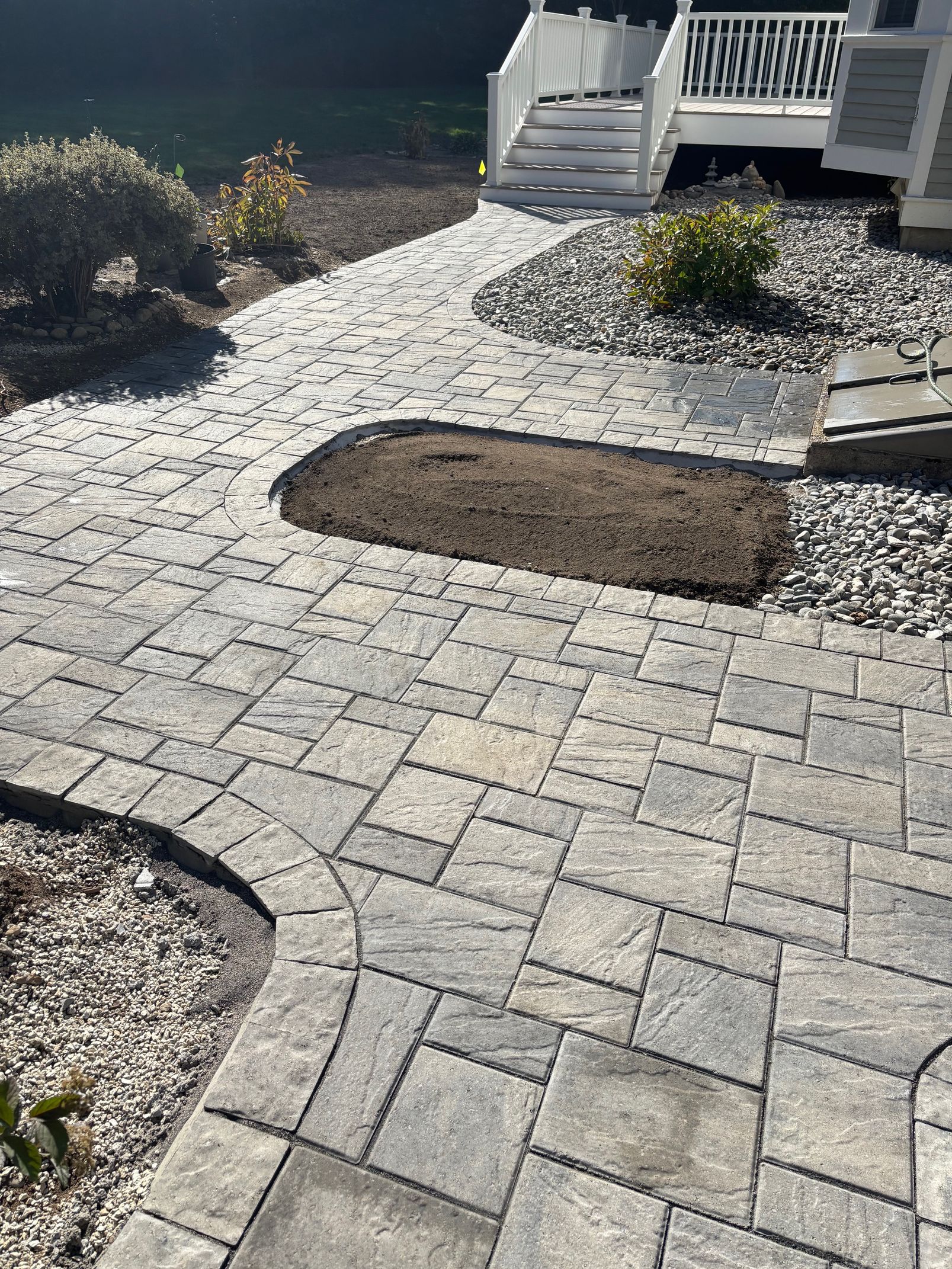 Stone paver walkway with a small, raised planting area, leading to a white porch with stairs.