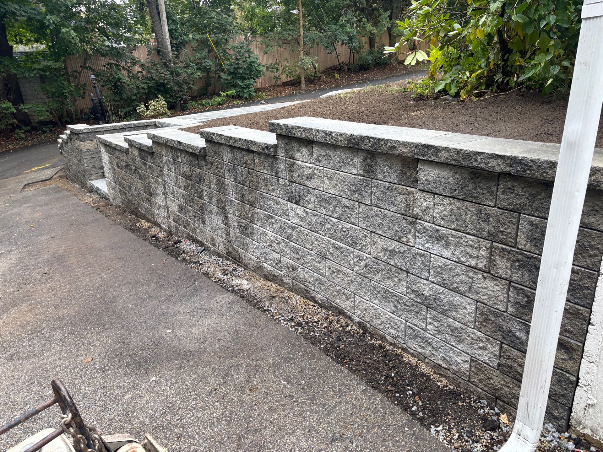 Gray brick retaining wall next to a paved driveway. Green trees in the background.