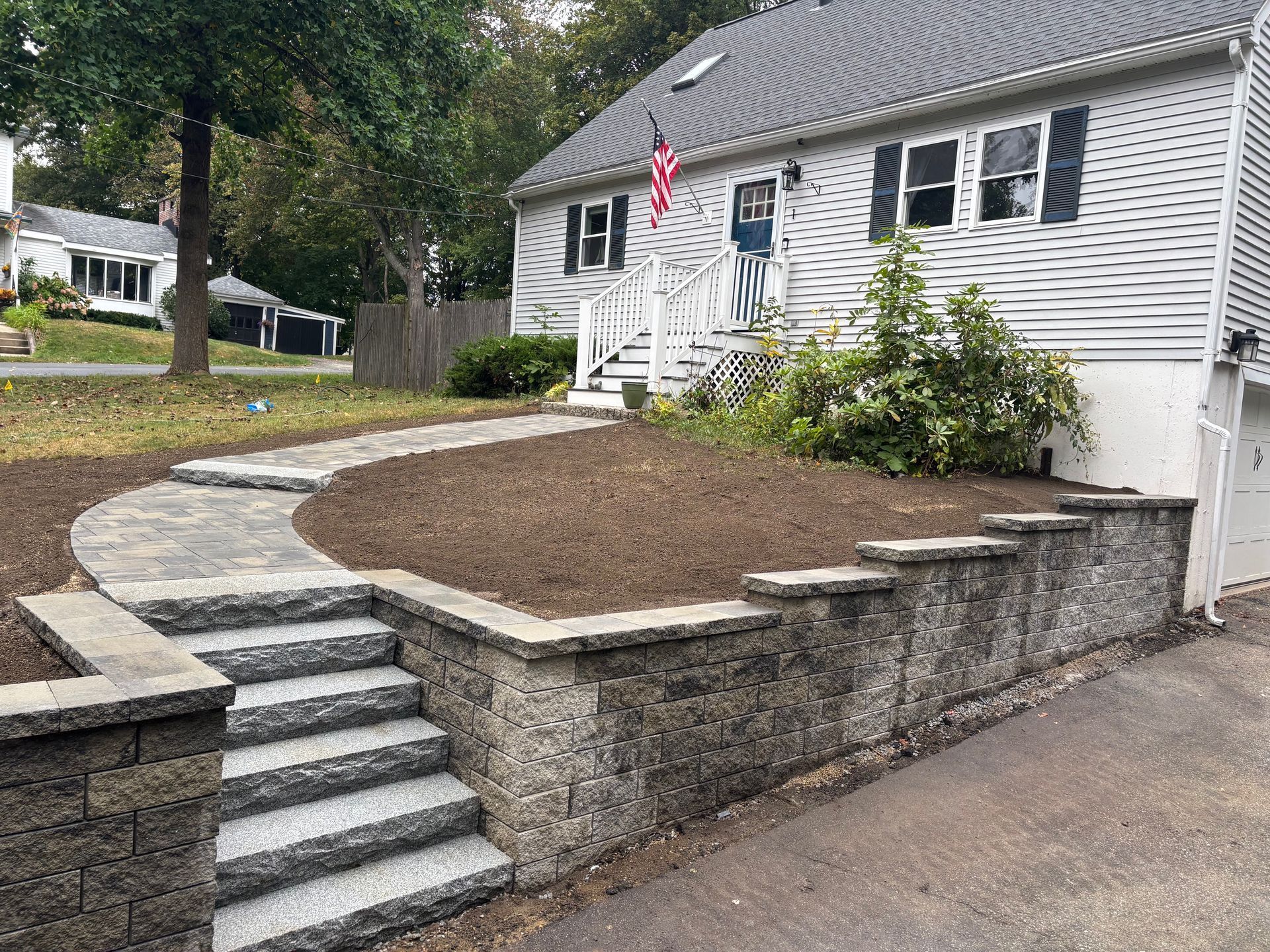 Stone steps and pathway lead to a house with a small American flag, flanked by a retaining wall.