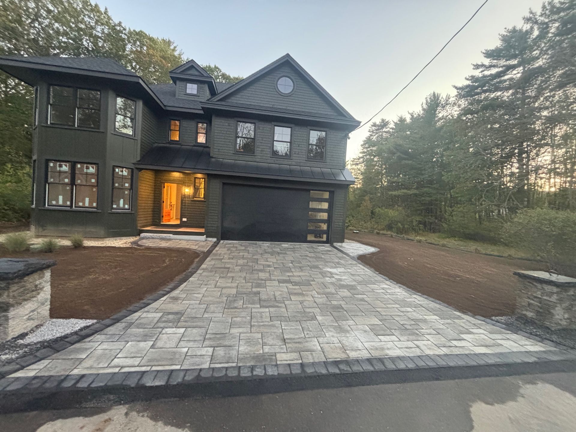 Dark green house with gray brick driveway.