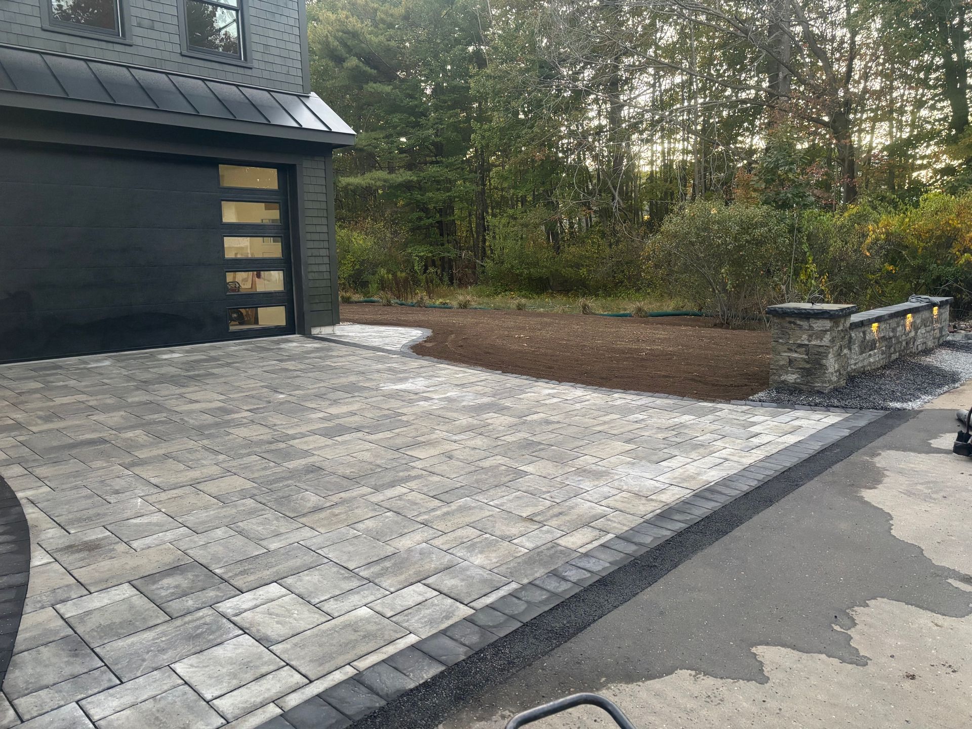 Paver driveway leading to a black garage with trees in the background.