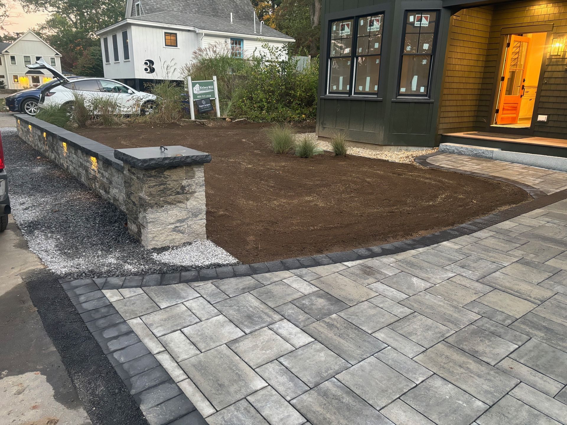 Stone paver walkway leading to a building with a newly landscaped bed and a stone retaining wall.