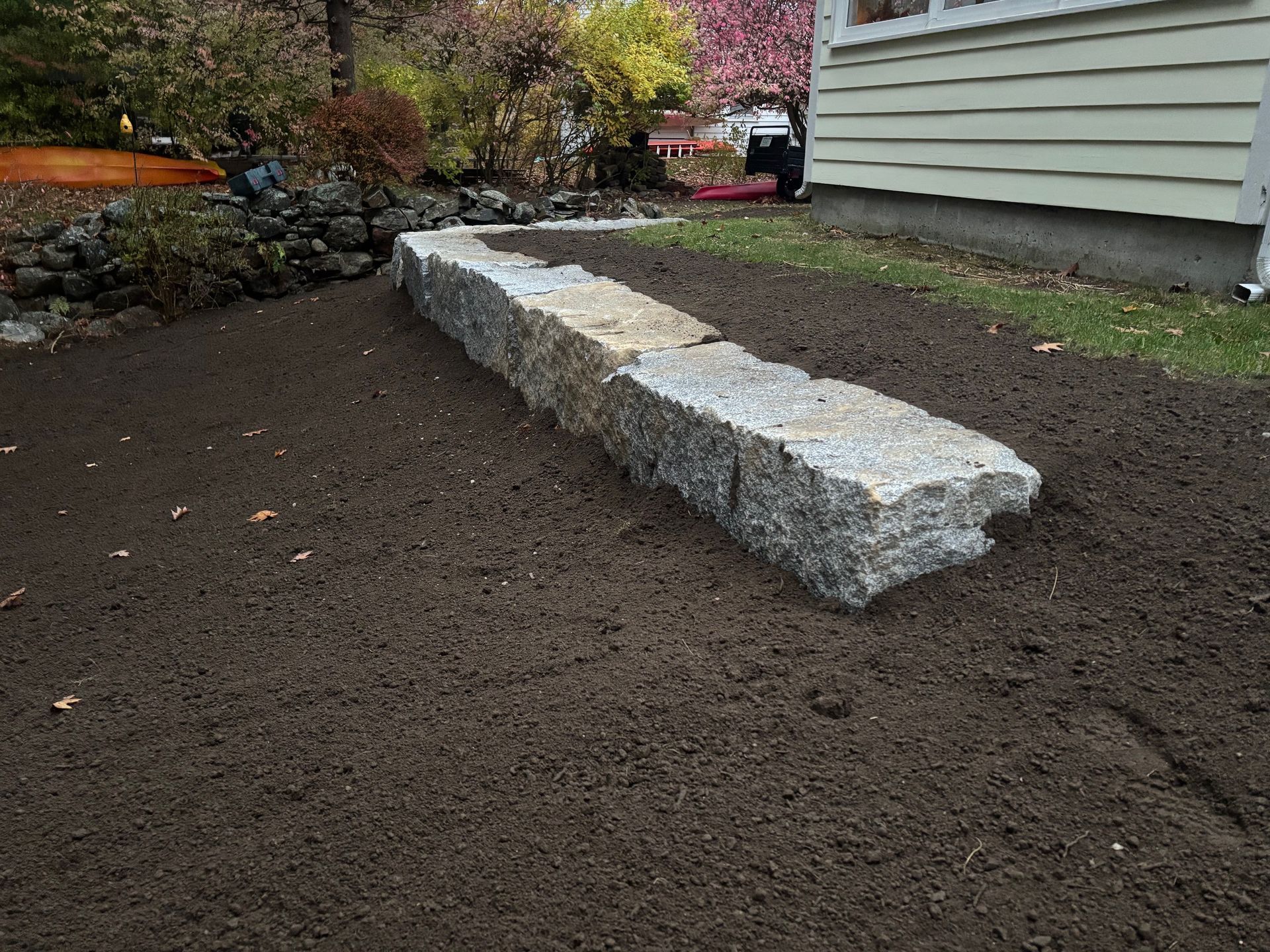 Granite retaining wall in a prepared garden bed next to a house.