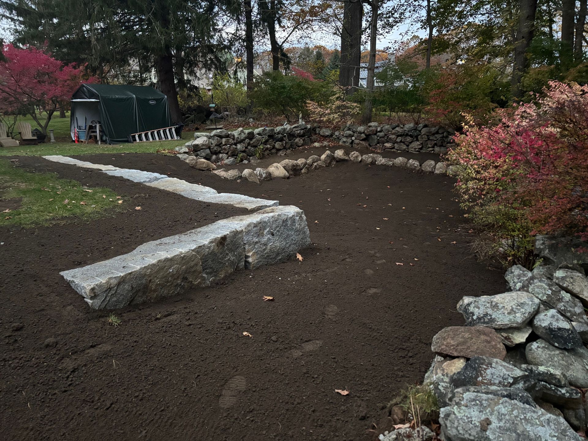 A garden area with dark soil and stone borders, with a path of large stone slabs.