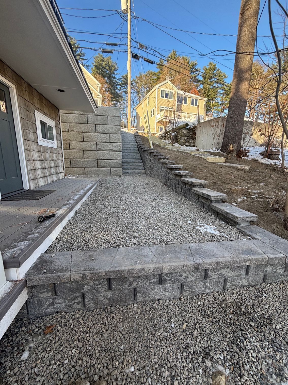 Stone retaining walls and steps leading uphill, graveled walkway in front of a house, sunny day.