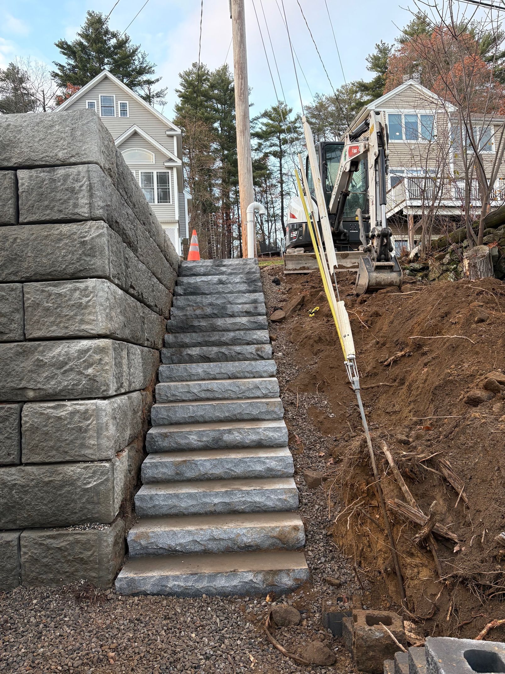 Stone staircase built alongside a retaining wall and dirt embankment, leading uphill between two houses.