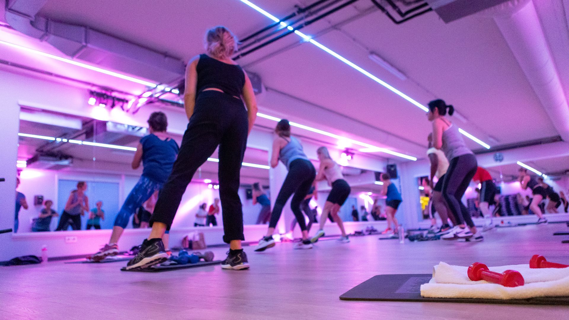 People exercising in a gym with mirrors, under purple and white lights.