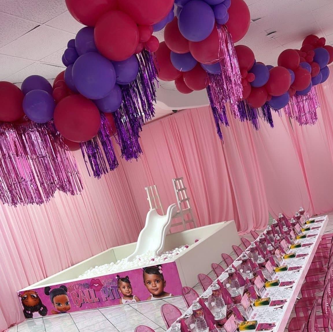 Pink and purple party decorations with balloons, a slide, and table settings.