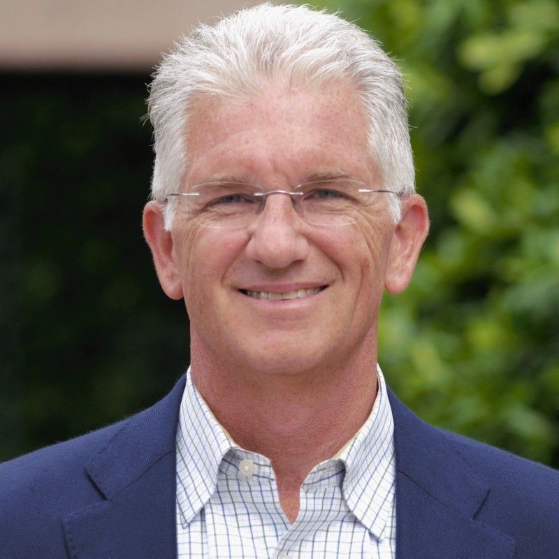 A man wearing glasses and a blue suit smiles for the camera